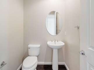 This powder room features a stylish pedestal sink with a modern faucet and an oval mirror, complemented by a sleek white toilet.