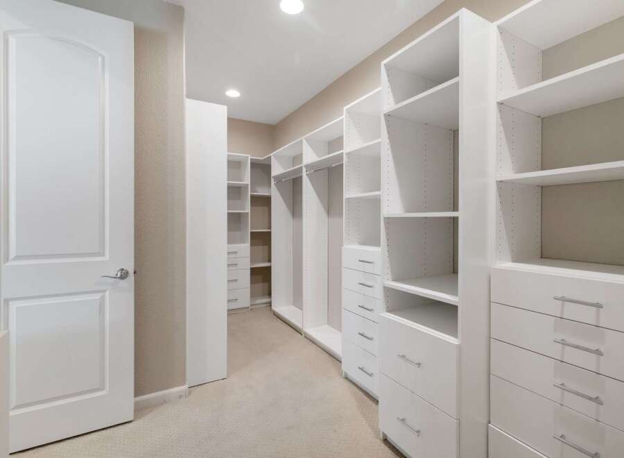 Step into this spacious walk-in closet, featuring custom white shelving and ample drawer space for organized storage.