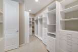 Step into this spacious walk-in closet, featuring custom white shelving and ample drawer space for organized storage.