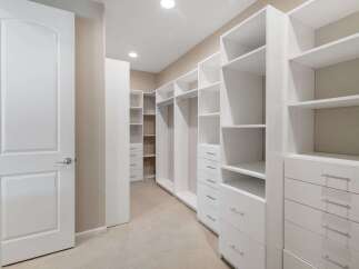 Step into this spacious walk-in closet, featuring custom white shelving and ample drawer space for organized storage.