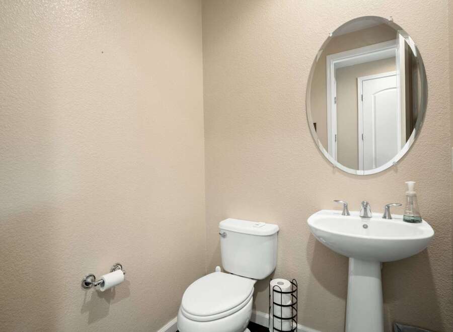 This powder room features a sleek pedestal sink with modern chrome fixtures, complemented by an elegant oval mirror above.