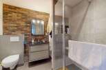This modern bathroom features a striking exposed brick accent wall, complemented by sleek grey tiles and a floating vanity.