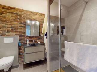 This modern bathroom features a striking exposed brick accent wall, complemented by sleek grey tiles and a floating vanity.