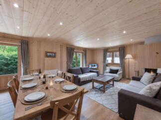 Experience cozy living in this charming wooden chalet, featuring a spacious dining area set for a delightful meal and a comfortable living room with a fireplace.