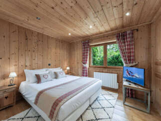 Experience cozy mountain living in this charming chalet bedroom, featuring warm wood paneling throughout and a comfortable king-sized bed adorned with decorative pillows.