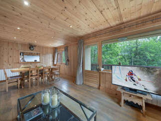 Experience cozy living in this charming wooden cabin, featuring a spacious dining area perfect for family meals and a large window offering scenic views.