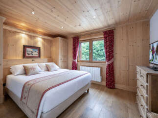 Experience cozy mountain living in this charming bedroom, featuring warm wood paneling throughout and a comfortable queen-sized bed adorned with decorative pillows.