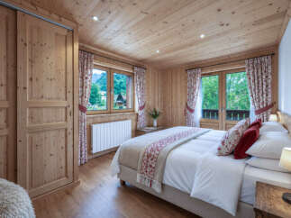 Experience cozy alpine living in this charming bedroom, featuring warm wood paneling throughout and a comfortable queen-sized bed adorned with decorative pillows.