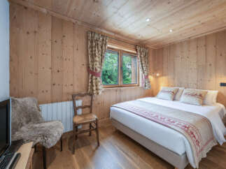 Experience cozy mountain living in this charming bedroom, featuring warm wood-paneled walls and a comfortable bed adorned with festive alpine-themed linens.