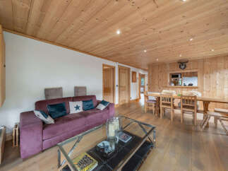 Experience cozy living in this charming wooden chalet, featuring a plush purple sofa and a spacious dining area perfect for gatherings.