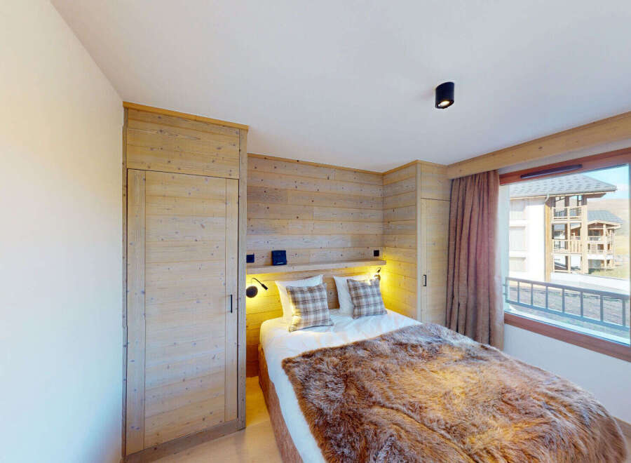 Experience cozy mountain living in this charming bedroom featuring a plush fur throw on the bed and warm wood paneling throughout.