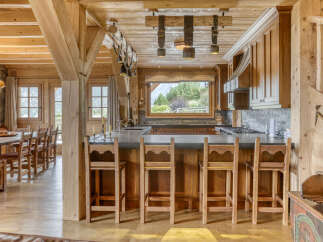 Experience rustic charm in this stunning mountain kitchen, featuring warm wooden beams, a spacious island with bar seating, and a picturesque window overlooking the scenic outdoors.