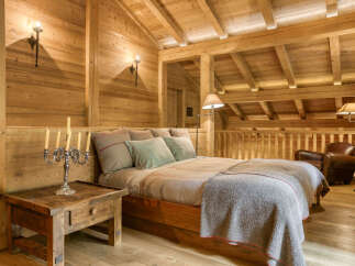 Experience rustic luxury in this charming wooden bedroom, featuring a cozy bed adorned with plush pillows and a warm throw blanket.