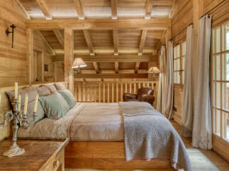 Experience rustic luxury in this charming wooden chalet bedroom, featuring a comfortable bed adorned with plush pillows and a cozy throw blanket.