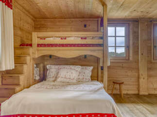 Experience cozy mountain living in this charming wooden cabin bedroom, featuring a space-saving bunk bed with playful red and white patterned bedding.
