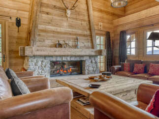 Experience rustic luxury in this stunning log cabin living room, featuring a grand stone fireplace and comfortable leather seating.
