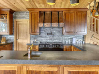 Experience rustic elegance in this mountain-style kitchen, featuring rich wooden cabinetry and a striking copper range hood.