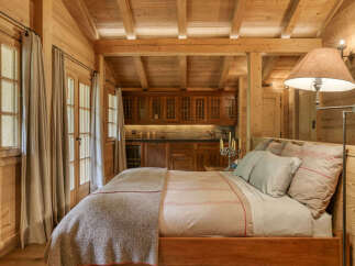 Experience rustic charm in this cozy wooden cabin bedroom, featuring a comfortable bed adorned with plush pillows and a warm throw blanket.