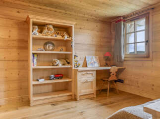 This charming wooden room features a tall bookshelf filled with toys and books, perfect for a child's play area or a cozy reading nook.
