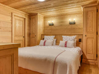 Experience rustic charm in this beautifully appointed wooden bedroom, featuring a cozy bed adorned with charming patterned linens and plush pillows.