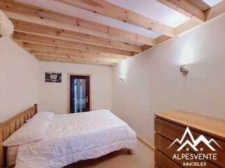 Discover this charming bedroom featuring a comfortable white bed, a wooden dresser, and exposed wooden ceiling beams that add a rustic touch.