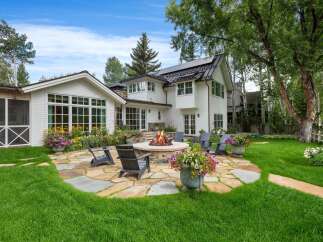 Experience outdoor living at its finest with this stunning backyard oasis, featuring a stone fire pit perfect for cozy evenings and surrounded by lush green lawns and vibrant flower arrangements.