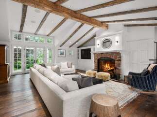 Experience rustic charm and modern comfort in this stunning living room, featuring exposed wooden beams and a grand brick fireplace.