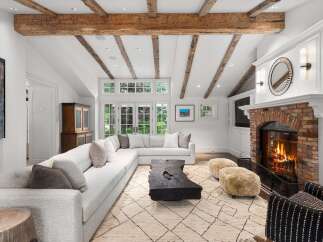 Experience rustic charm and modern comfort in this spacious living room, featuring exposed wooden beams and a cozy brick fireplace.