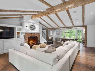 Experience rustic elegance in this spacious living room, featuring exposed wooden beams and a grand brick fireplace.