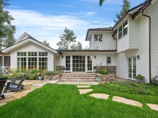 This stunning white home features a beautiful backyard with lush green grass and a stone pathway leading to a patio area.