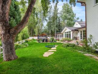 Enjoy outdoor living in this stunning backyard featuring a lush green lawn, a cozy fire pit area with seating, and a unique rope swing for added fun.