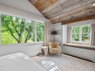 Experience serene living in this charming bedroom, bathed in natural light from expansive windows overlooking lush greenery.