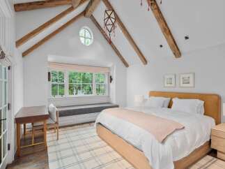 Experience rustic charm and modern comfort in this inviting bedroom, featuring exposed wooden beams and a cozy window seat overlooking lush greenery.
