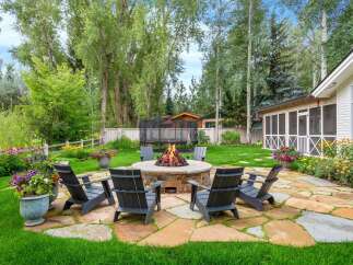 Experience outdoor living at its finest with this inviting backyard oasis, featuring a cozy stone fire pit surrounded by comfortable Adirondack chairs, perfect for gathering with loved ones.
