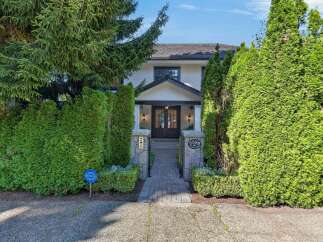 Discover this charming residence featuring a welcoming entryway framed by lush greenery and mature trees.