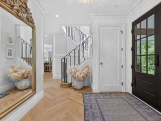 Step into a grand foyer featuring a stunning gold ornate mirror reflecting the elegant staircase with black wrought iron railings.
