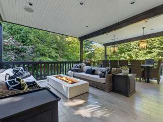 Experience ultimate outdoor living on this covered patio, featuring a modern gas fire pit and comfortable wicker seating.