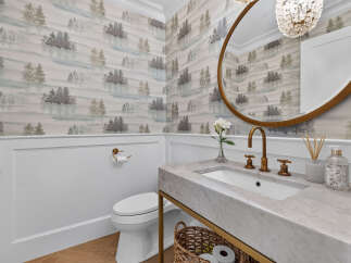 This powder room features a striking forest-themed wallpaper complemented by crisp white wainscoting.