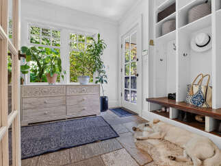 Welcome guests into this charming mudroom featuring a large window with lush greenery views and a built-in storage bench with cubbies.