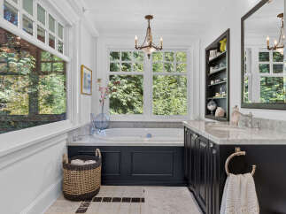 Indulge in luxury in this stunning bathroom featuring a deep soaking tub surrounded by marble countertops and a dark navy vanity.