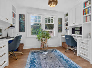 This bright and airy home office features two matching white built-in desks with brass hardware, each equipped with a black desk lamp and a computer.