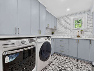 Discover this beautifully renovated laundry room featuring sleek, light blue cabinetry with modern gold hardware, complemented by a classic white subway tile backsplash.