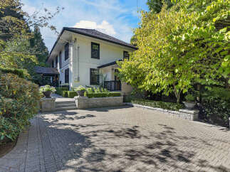 Discover this charming white house with classic dark trim, set amidst lush greenery and mature trees.