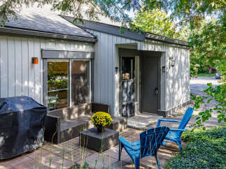 Enjoy outdoor living with this charming patio featuring a covered grill, comfortable wicker seating, and vibrant yellow mums.