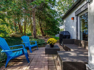Enjoy outdoor living with this charming patio featuring vibrant blue Adirondack chairs and a comfortable wicker sectional.