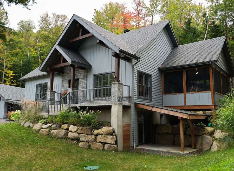 Discover this stunning modern home nestled in a serene forest setting, featuring a striking combination of gray siding and natural stone accents.