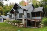 Discover this stunning modern home nestled in a serene forest setting, featuring a striking combination of gray siding and natural stone accents.