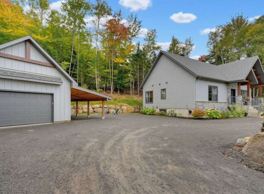 Discover this stunning property featuring a modern gray-sided home with stone accents, complemented by a detached garage and a charming carport.