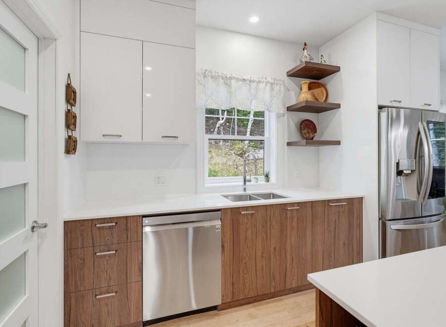 Discover this modern kitchen featuring sleek white cabinetry and warm wood lower cabinets, complemented by a double-basin sink and a stainless steel dishwasher.