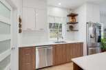 Discover this modern kitchen featuring sleek white cabinetry and warm wood lower cabinets, complemented by a double-basin sink and a stainless steel dishwasher.
